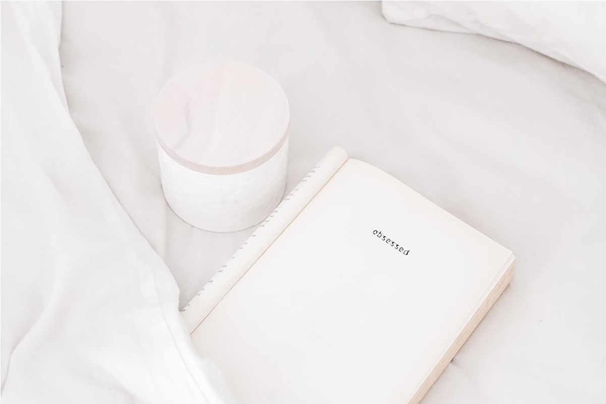 Open book with 'obsessed' written, next to a closed jar on a white sheet.